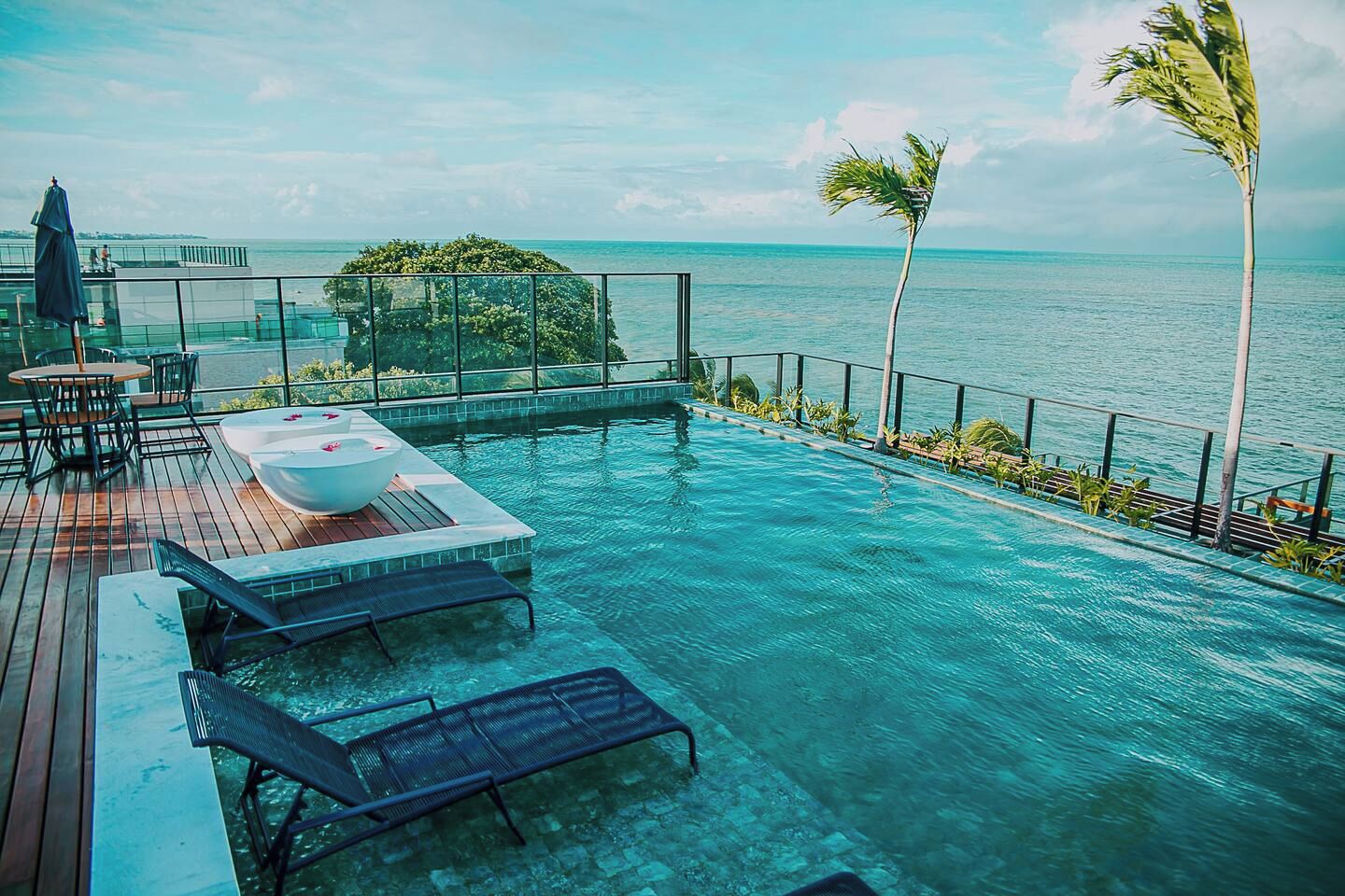 Uma piscina infinita com espreguiçadeiras, uma banheira de hidromassagem e vista para o oceano.