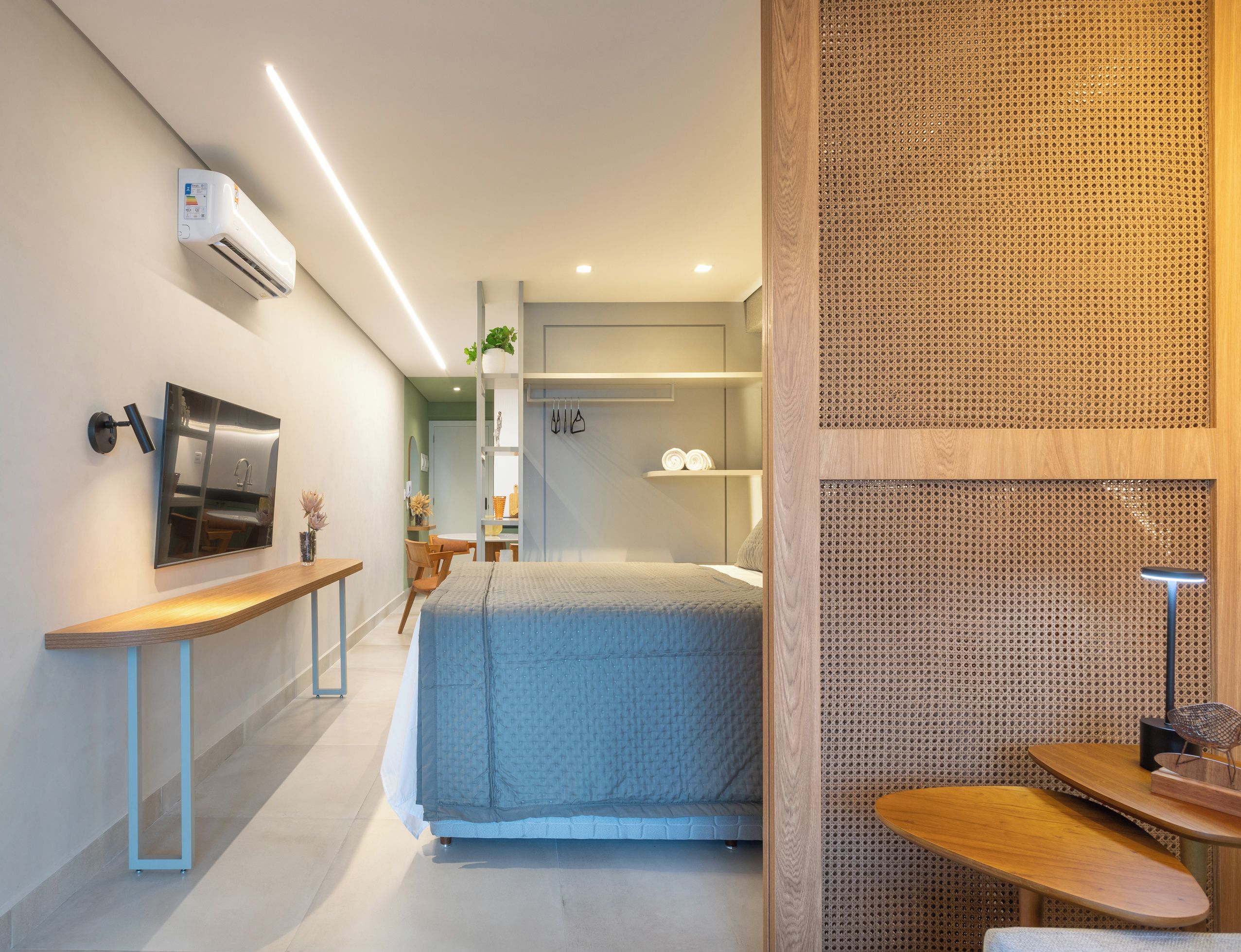 Quarto de hotel moderno com cama, mesa de cabeceira e televisão montada na parede.