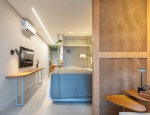 Quarto de hotel moderno com cama, mesa de cabeceira e televisão montada na parede.