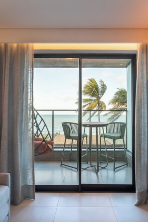 Quarto com porta de vidro deslizante que dá para uma varanda com vista para o mar e palmeiras.