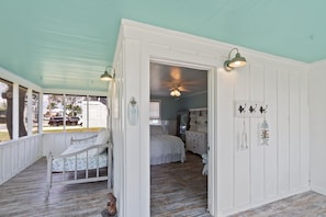 A room with a bed, a dresser, and a chair. There is a door leading to another room. - Bayou Belle - Bear Point 2 BR Cottage - Orange Beach - 14 Day Min Stay (Orange Beach)