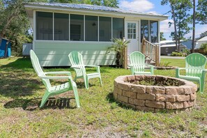 A house with a screened porch, a fire pit, and three green chairs. - Bayou Belle - Bear Point 2 BR Cottage - Orange Beach - 14 Day Min Stay (Orange Beach)
