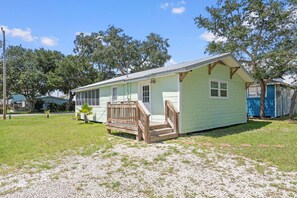 A small, single-story house with a porch and a small deck, surrounded by grass and trees. - Bayou Belle - Bear Point 2 BR Cottage - Orange Beach - 14 Day Min Stay (Orange Beach)