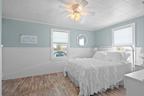 Un dormitorio con cama, ventilador de techo, ventana con vista y un cartel en la pared.