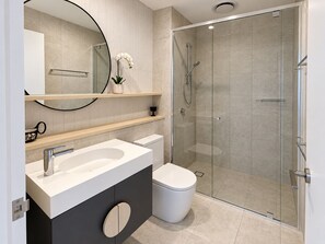 Moderni kylpyhuone, jossa on lasiseinällä varustettu suihku, valkoinen pesuallas ja wc.