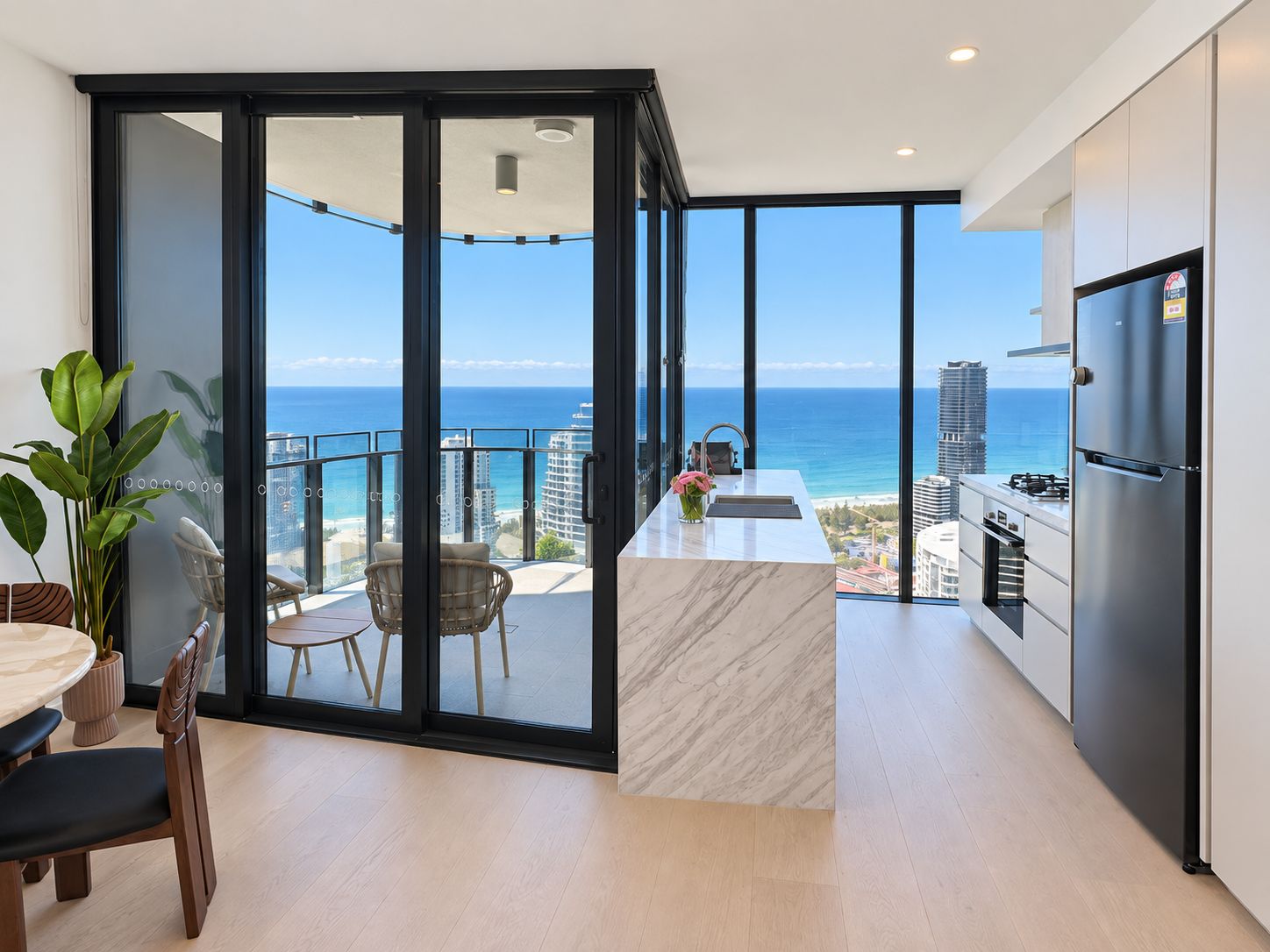 A modern kitchen with a view of the ocean, a dining area with a table and chairs, and a balcony with a chair.
