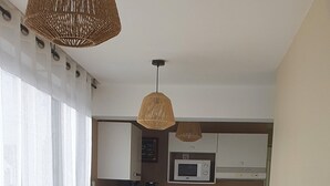 Eine moderne Küche mit Essbereich, ausgestattet mit einem Holztisch und -stühlen, einer gewebten Pendelleuchte und Blick zum Wohnbereich.