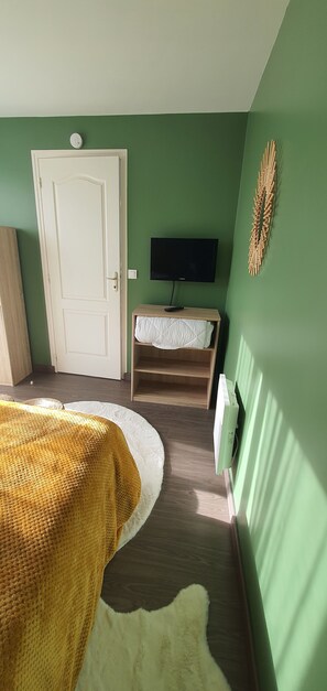 A room with a bed, a television on a stand, a door, and a radiator. - Vrbo Property (Fort-Mahon-Plage)