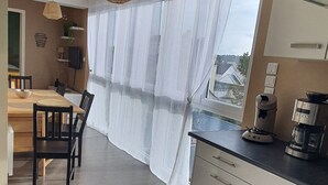 Eine moderne Küche mit eingebautem Herd, ein Essbereich mit Tisch und Stühlen sowie ein Blick durch leichte Vorhänge.