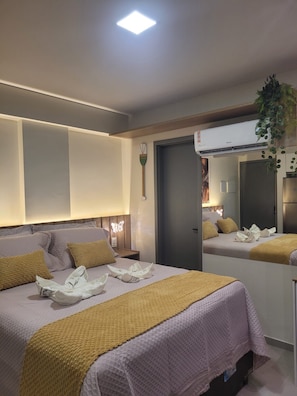 Ein Hotelzimmer mit zwei Betten, einem Nachttisch, einem Spiegel, einer Wand-Klimaanlage und einer Deckenleuchte.