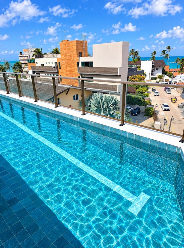 Ein Schwimmbad mit klarem, blauem Wasser, umgeben von einem modernen Gebäude mit flachem Dach und einem Balkon.