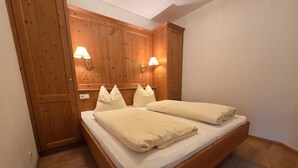 A wooden bed with two pillows and a blanket, a wooden wardrobe, and two wall-mounted lamps. - Cozy Holiday Apartment (Achenkirch)