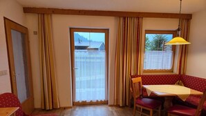 A room with a dining area featuring a table and chairs, a bench, and a window with curtains. - Cozy Holiday Apartment (Achenkirch)