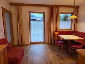 A room with a dining area featuring a table and chairs, a bench, and a window with curtains. - Cozy Holiday Apartment (Achenkirch)