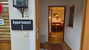 A hallway leading to a dining area with a table and chairs, a sign indicating 'Appartement 1', and a door with a handle. - Cozy Holiday Apartment (Achenkirch)