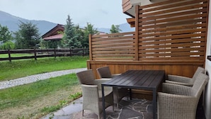 An outdoor patio with a stone table and wicker chairs, a wooden fence, and a view of a mountain. - Cozy Holiday Apartment (Achenkirch)