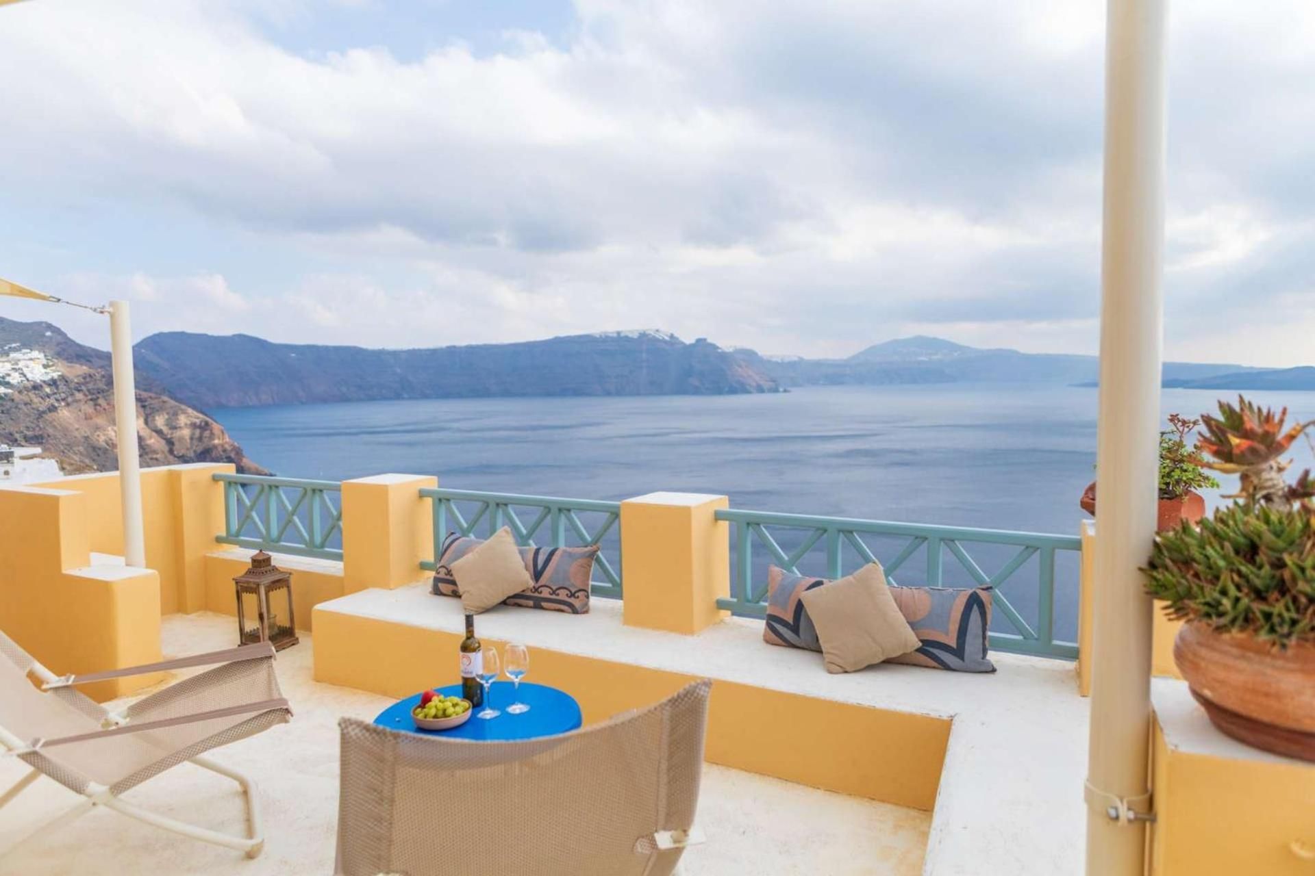 A terrace with a view of the sea, a table with a bottle and glasses, and a chair.