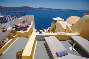 A terrace with lounge chairs, a table with fruits, and a view of the sea. - Zoe Aegeas Traditional Houses (Santorini)