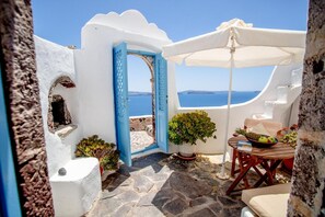 A white-walled outdoor area with a blue door, a table with fruits, and a view of the sea. - Zoe Aegeas Traditional Houses (Santorini)