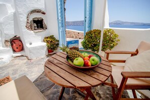 A wooden table with a bowl of fruit and a book titled 'Greece' on a balcony with a view of the sea. - Zoe Aegeas Traditional Houses (Santorini)
