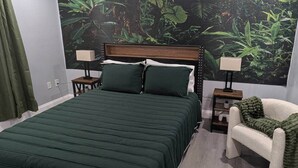 Ein Schlafzimmer mit einem Bett, zwei Nachttischen, einem Sessel und einem Wandbild von einem Dschungel.