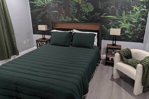 A bedroom with a bed, two bedside tables, a chair, and a mural of a jungle. - Whispers of the Jungle (Combee Settlement)