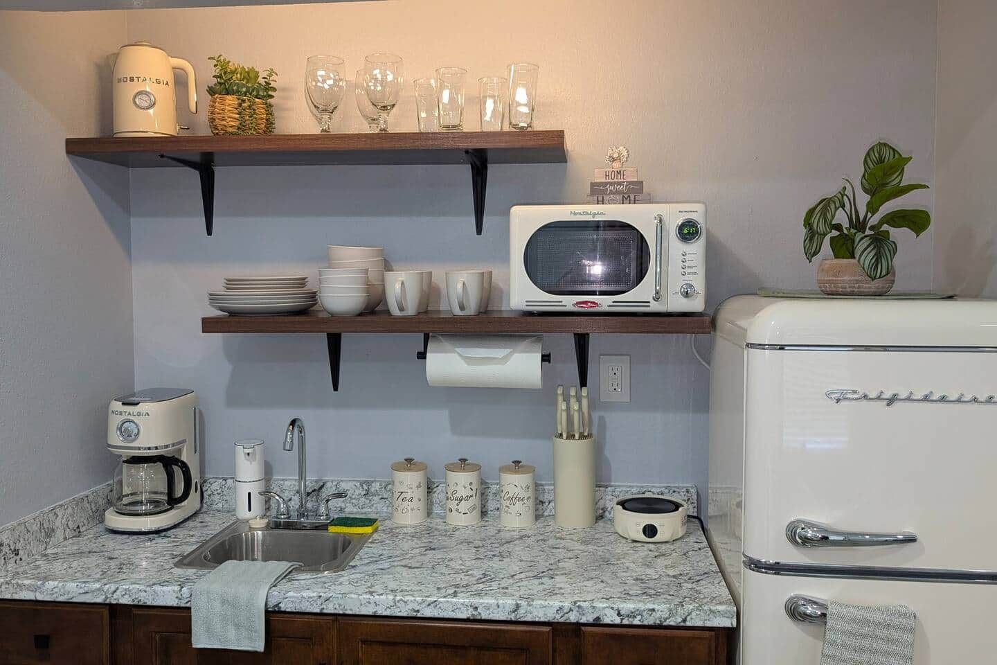 Eine Küche mit Mikrowelle, Kühlschrank, Kaffeemaschine und Regalen mit Geschirr und Gläsern.