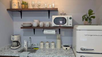 Eine Küche mit Mikrowelle, Kühlschrank, Kaffeemaschine und Regalen mit Geschirr und Gläsern.