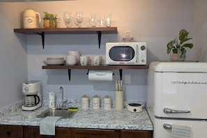 A kitchen with a microwave, refrigerator, coffee maker, and shelves with dishes and glasses.
