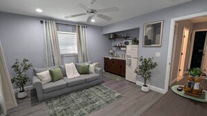 Ein gemütlicher, kompakter Wohnraum mit grauem Sofa, einer kleinen Küchenzeile und einem Esstisch.