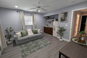 A compact living space with a grey sofa, a small kitchen area, and a dining table. - Whispers of the Jungle (Combee Settlement)