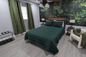 A bedroom with a bed, a nightstand, a chair, and a window with curtains.
