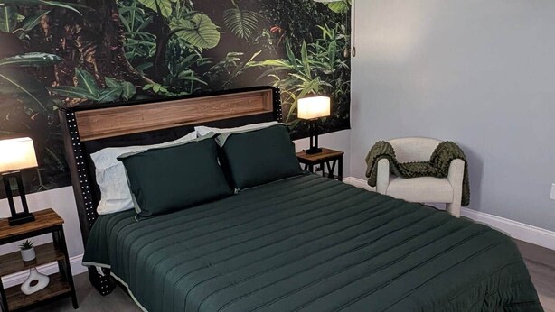 Ein Schlafzimmer mit einem Bett, zwei Nachttischen, einem Sessel und einer Wandmalerei.