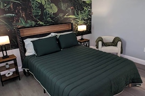 Un dormitorio con una cama, dos mesitas de noche, una silla y un mural en la pared.
