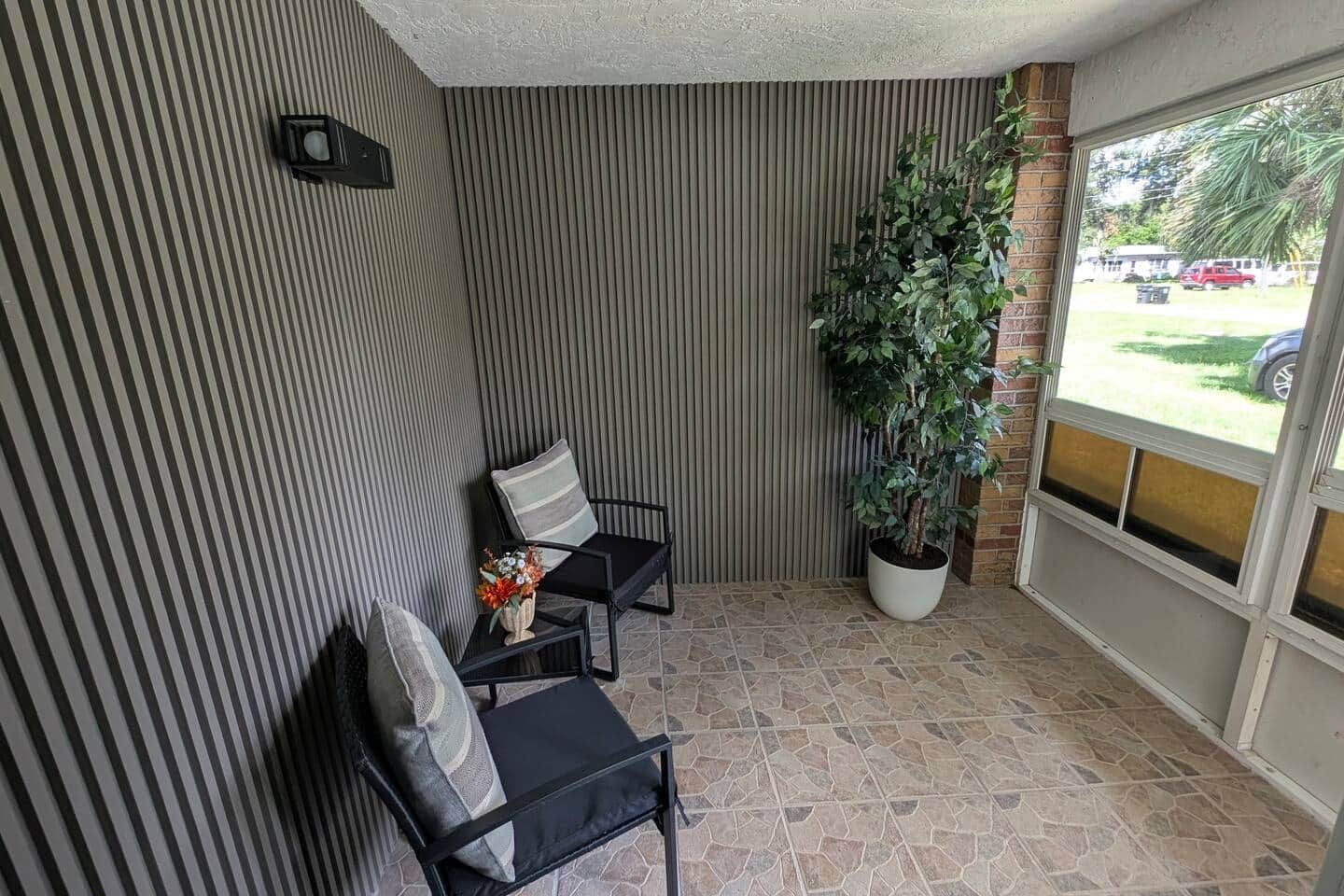 Ein kleiner, abgeschlossener Patio-Bereich mit gestreiften Wänden, zwei Stühlen, einem Blumentopf und Blick durch eine Glastür.
