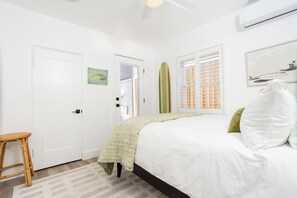 Een slaapkamer met een bed, een stoel, een raam met jaloezieën en een wandairconditioner.