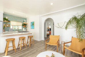 Eine moderne Küche mit Bar und Sitzgelegenheit, einem Esstisch mit Stühlen sowie ein Wohnbereich mit Sofa und Sesseln.