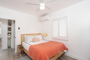 Een slaapkamer met een bed, een plafondventilator, een airconditioner, een bedlamp en een raam met luiken.