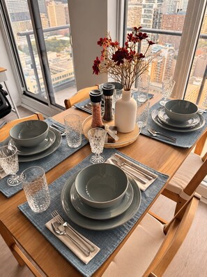 A dining table set with plates, glasses, cutlery, and a vase with flowers. - Modern Downtown Toronto Studio with Balcony & Stunning City Views. (Toronto)