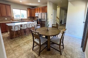 A kitchen with wooden cabinets, a central island with bar stools, a dining table with chairs, and a refrigerator. - Colorado Springs Family Retreat 4BR, Game Loft & Garage (Colorado Springs)