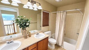 Une salle de bain avec deux lavabos, des toilettes, une baignoire et un rideau de douche.
