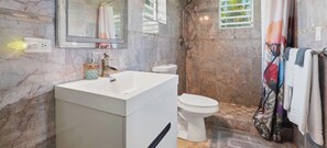 Un bagno con una parete in marmo, un lavandino bianco, un water e una zona doccia.