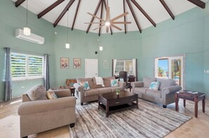 A spacious living room with a high ceiling, a ceiling fan, and a large window with shutters. - Luxury 1 bedroom Waterfront Villa with Private Pool and Spacious Deck (Frederiksted)