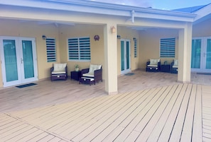 A covered outdoor seating area with two wicker chairs and a small table, a door with glass panels, and a wall-mounted light fixture. - Luxury 1 bedroom Waterfront Villa with Private Pool and Spacious Deck (Frederiksted)