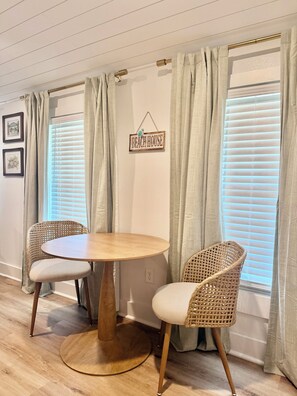 A dining area with a round wooden table and two wicker chairs, a wall-mounted sign reading 'BEACHHOUSE', and a window with blinds. - 3BR Coastal Cottage - Steps to St. Joseph Bay (Port St. Joe)