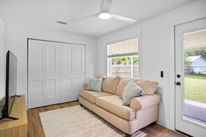 A room with a beige sofa, a television on a stand, a ceiling fan, and a door with a view of the outside. - 3BR Coastal Cottage - Steps to St. Joseph Bay (Port St. Joe)