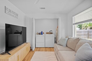 A compact living space with a television, washing machine, and a sofa. - 3BR Coastal Cottage - Steps to St. Joseph Bay (Port St. Joe)