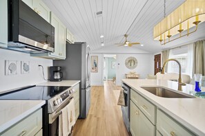 A modern kitchen with stainless steel appliances, a central island, and a view into the dining area. - 3BR Coastal Cottage - Steps to St. Joseph Bay (Port St. Joe)