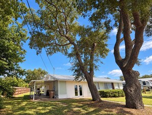 A single-story house with a covered porch, a garage, and a yard with trees. - 3BR Coastal Cottage - Steps to St. Joseph Bay (Port St. Joe)