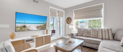 A living room with a large TV, a sofa, a coffee table, and a view of the outdoors.